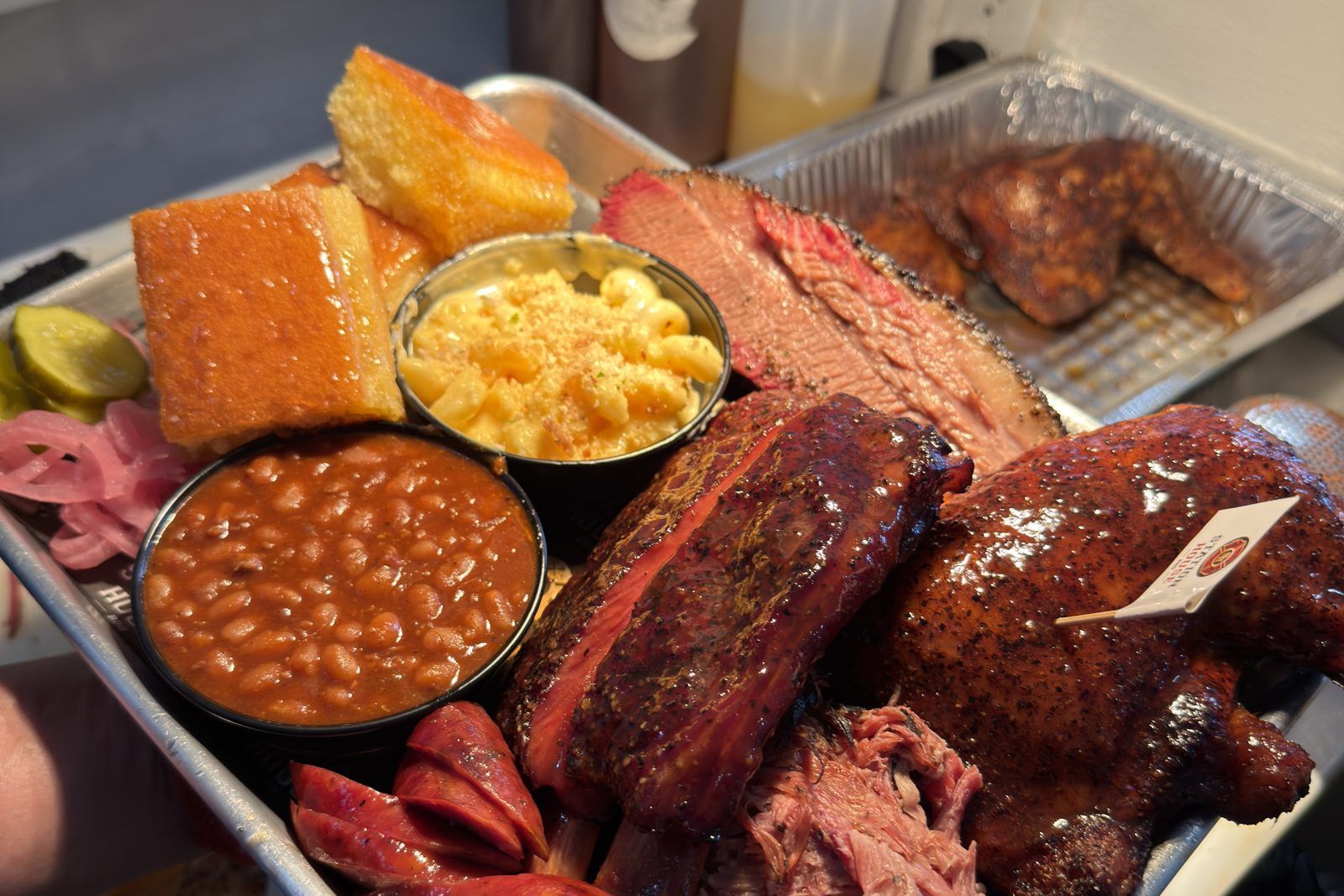 A Station House BBQ platter of brisket, ribs, chicken, sausage, and pulled pork with Smoked Gouda Mac & Cheese, Cowboy Baked Beans, and cornbread