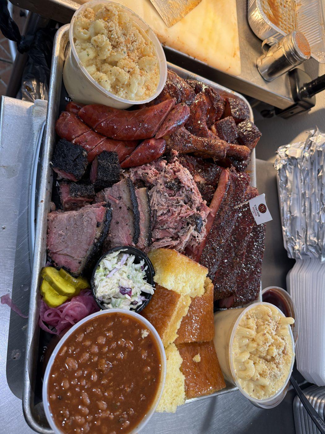 A Station House BBQ tray with sliced brisket, Smoked Gouda Mac and Cheese, Cowboy Baked Beans, and cornbread
