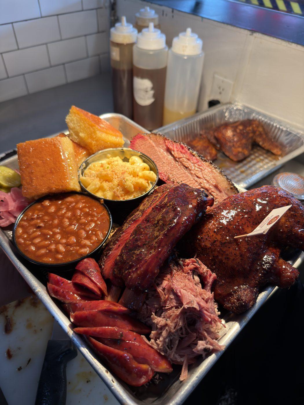 A Station House BBQ tray with brisket, ribs, sausage, pulled pork, chicken, mac and cheese, and baked beans