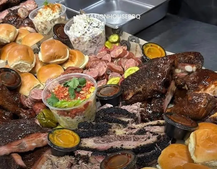 A large spread of smoked brisket, ribs, sausage, rolls, slaw and sauces